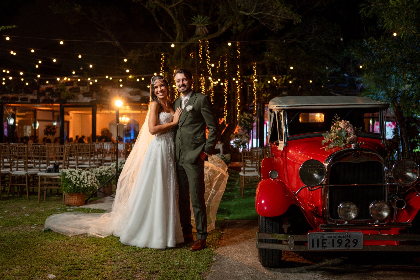 Noivos ao lado do carro antigo no jardim iluminado